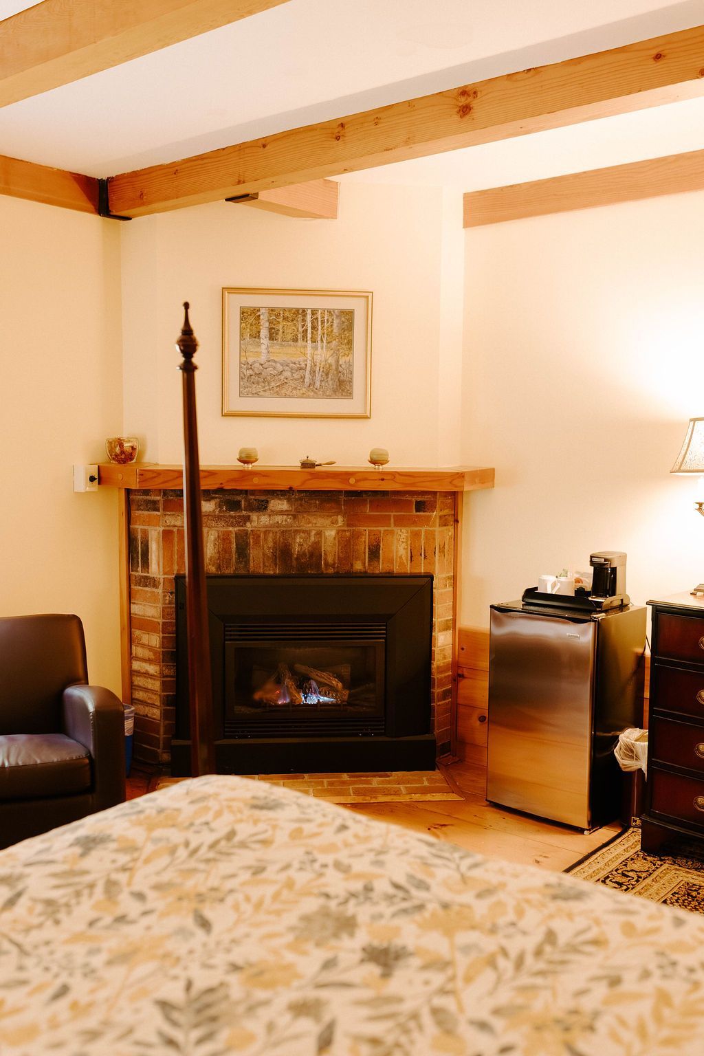 Cozy living room with a brick fireplace, wooden beam ceiling, and patterned bedspread in the foreground