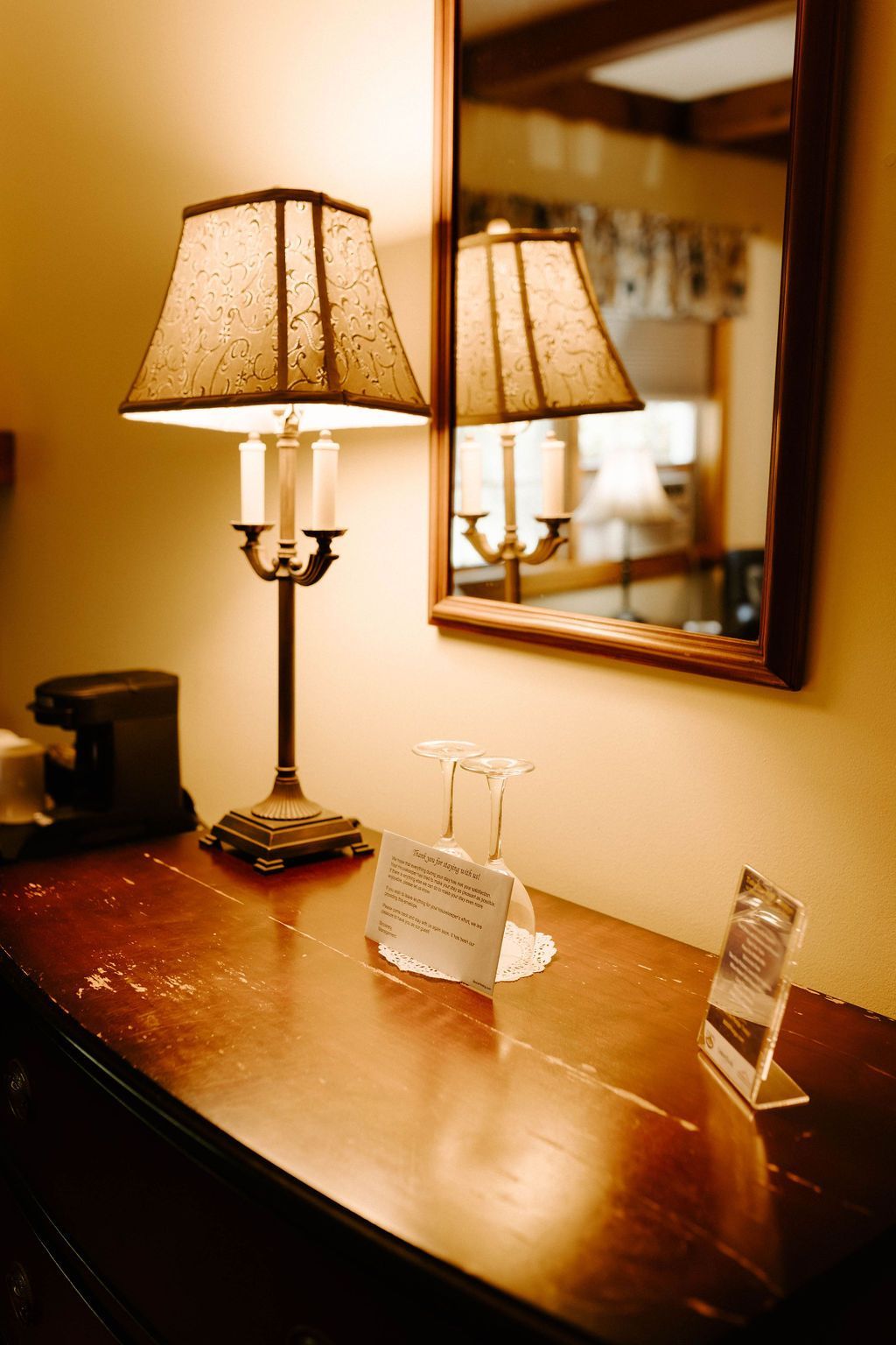 Lamp-lit wooden desk with a mirror, business card holder, and small framed photo in a warm room.