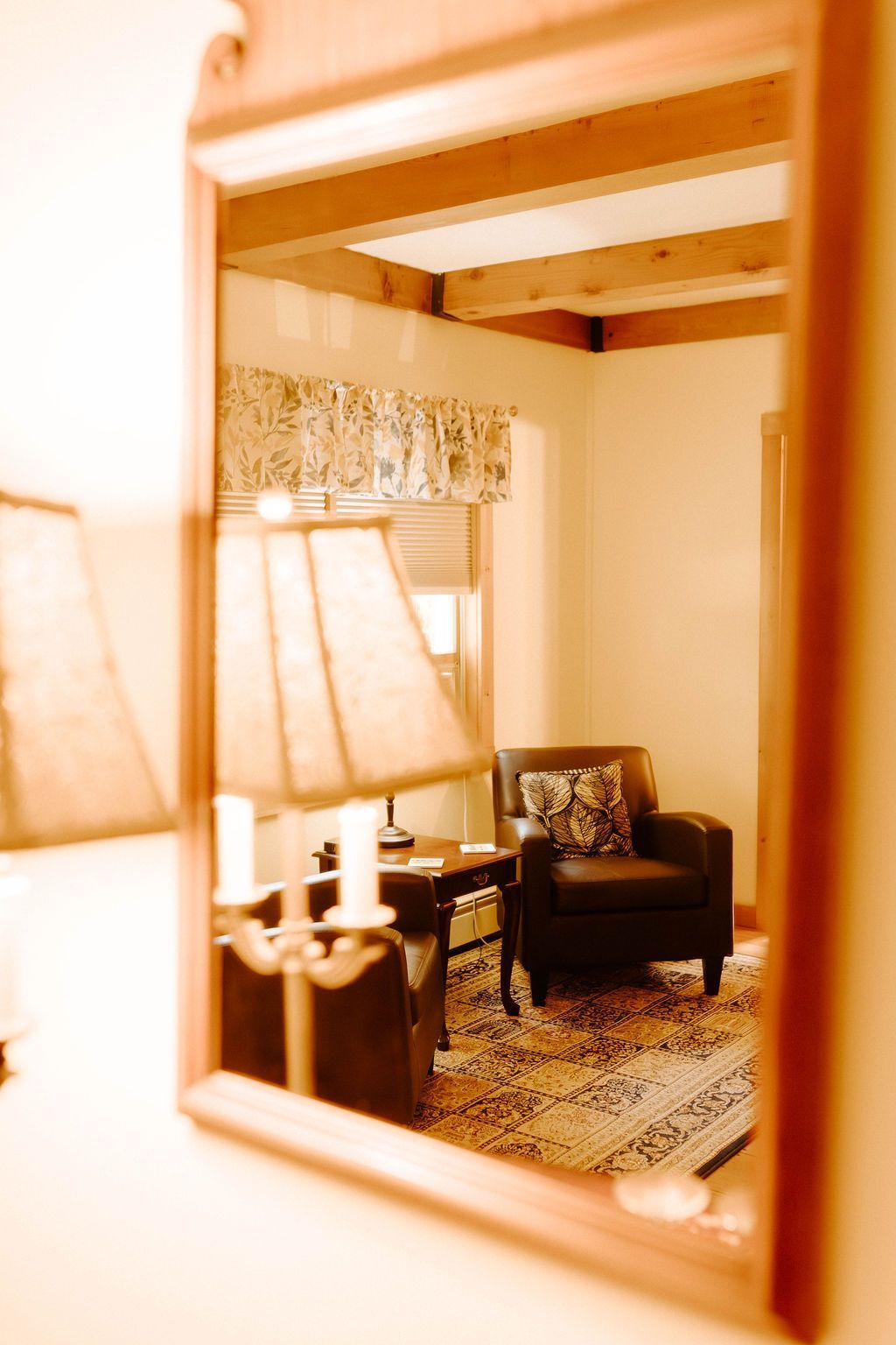 Mirror reflecting a cozy living room with lamp, armchair, window, and patterned rug