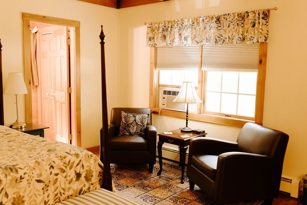 Hotel room with two black chairs by a window, a small table, and a bed on the left.