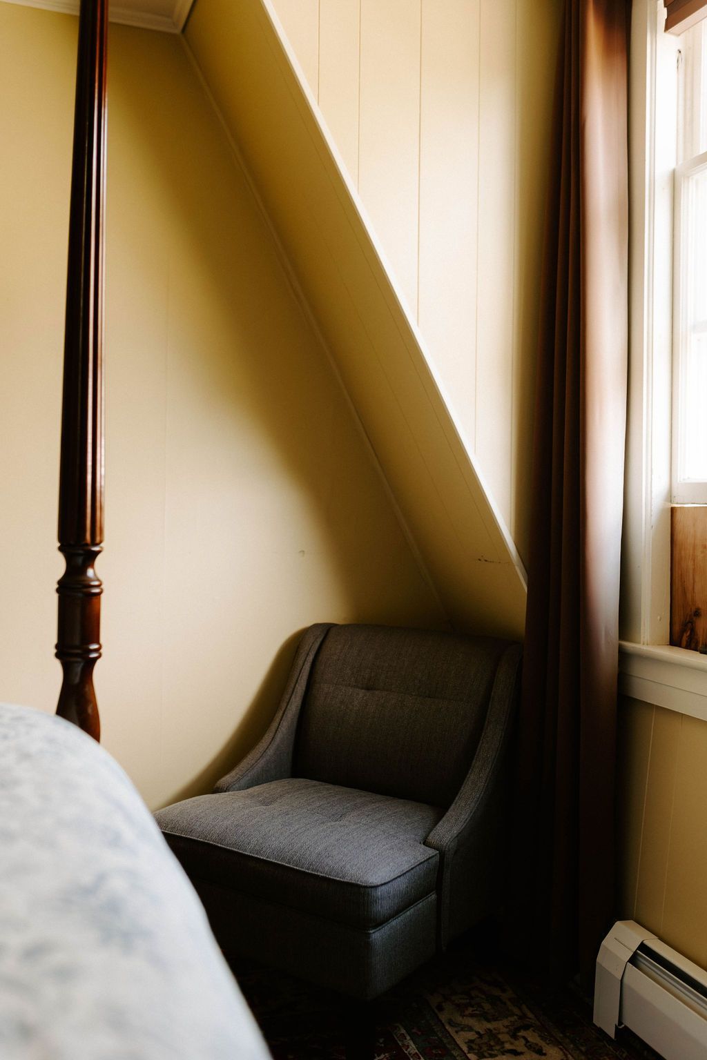 Small gray chair in a yellow room beside a window and radiator