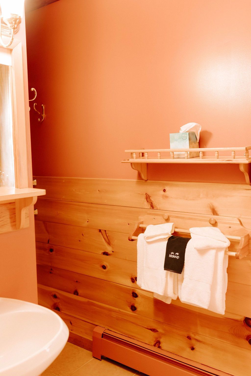 Wood-paneled bathroom with peach walls, a sink, and towels hanging on a rack.