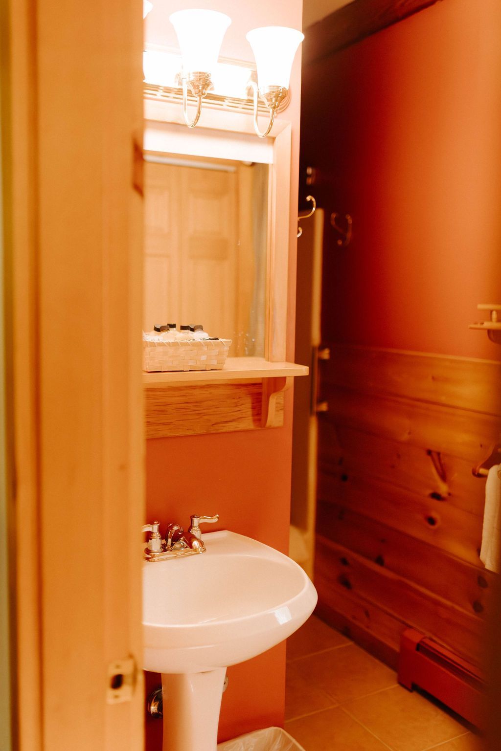Small bathroom with a pedestal sink, mirror, and warm wood-paneled walls.