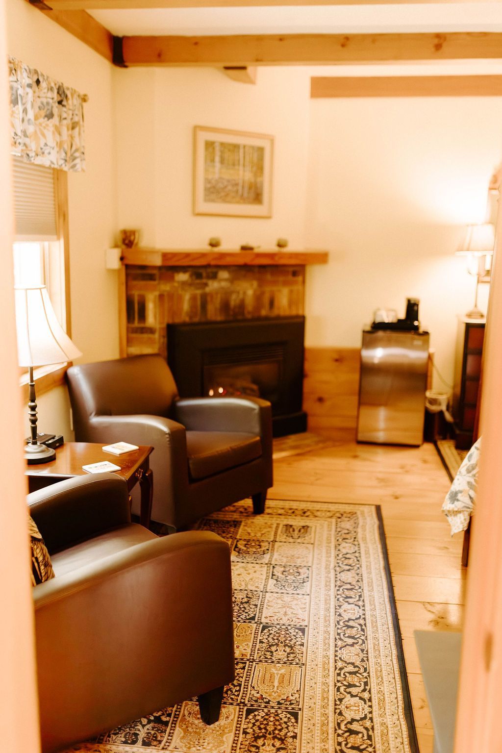 Cozy living room with leather chairs, fireplace, patterned rug, and exposed wood beams.