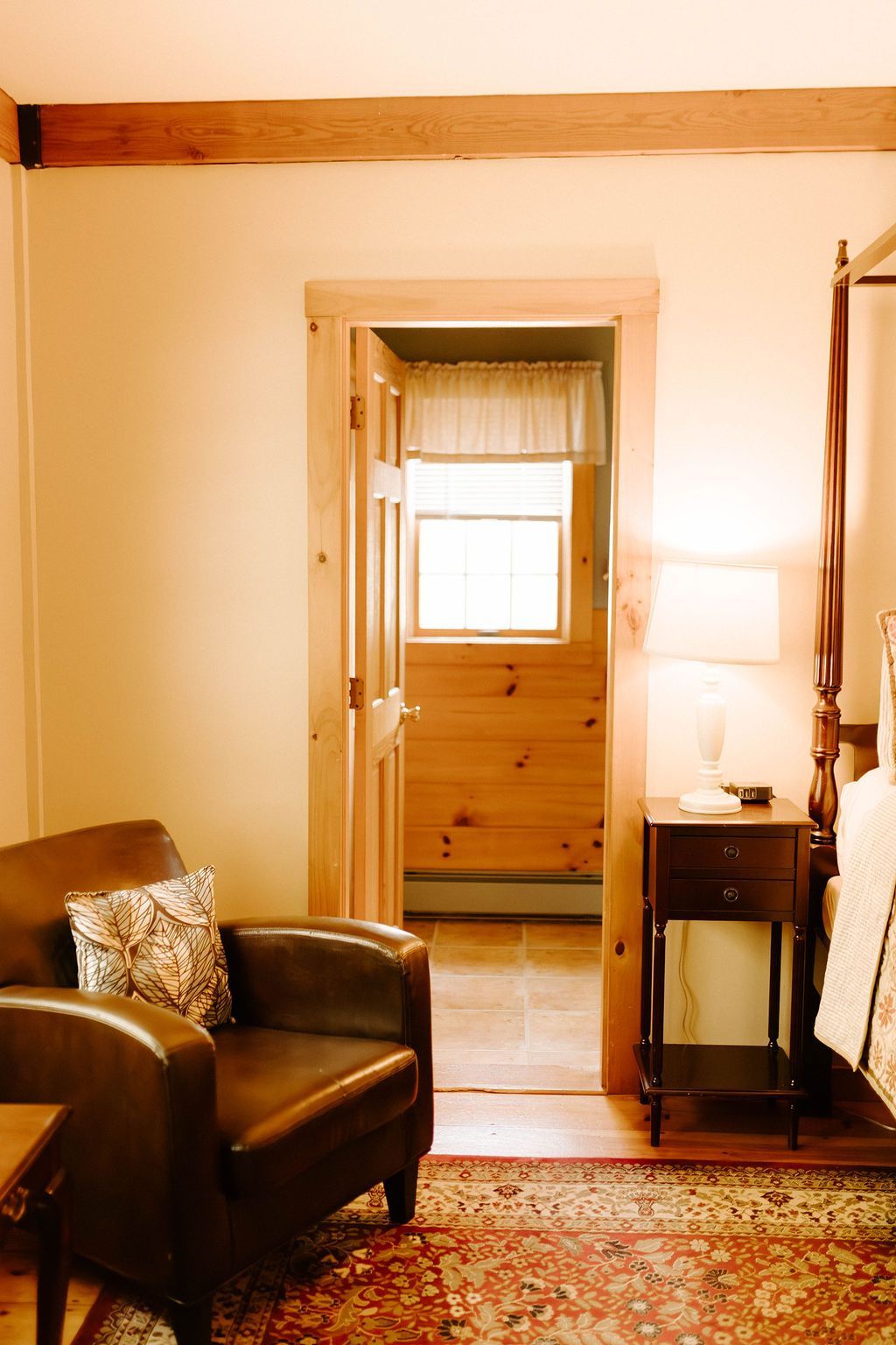 Cozy living room with leather chair, patterned rug, wooden trim, and doorway to a bright bedroom