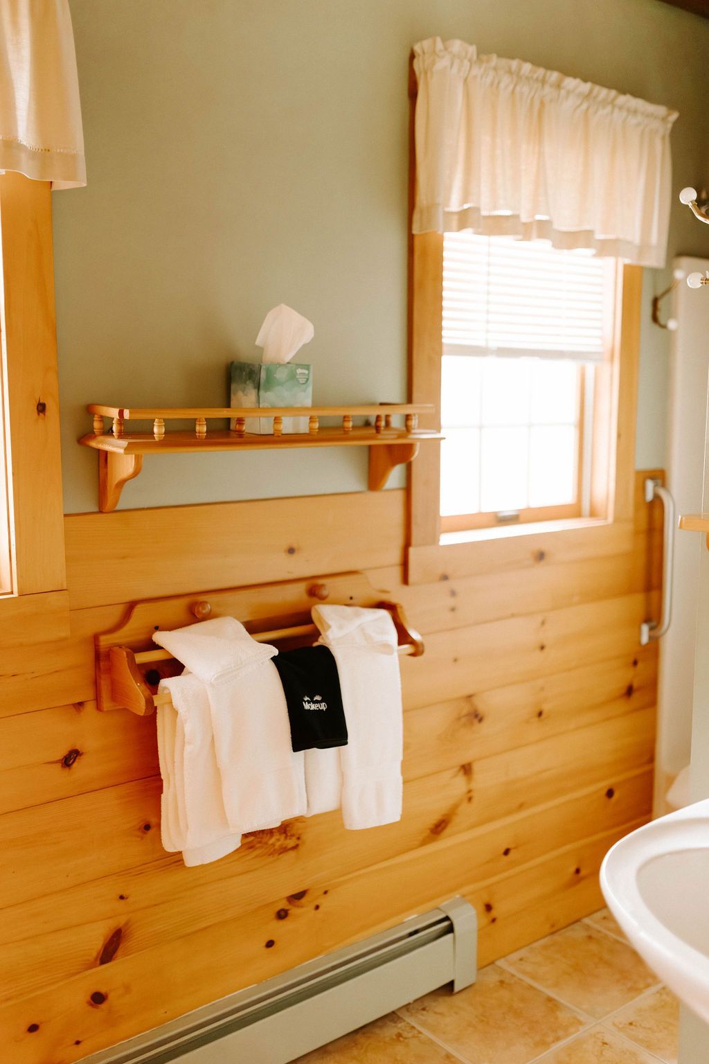 Bathroom with pine wainscoting, window shelf, hanging towels, and a sink at right.