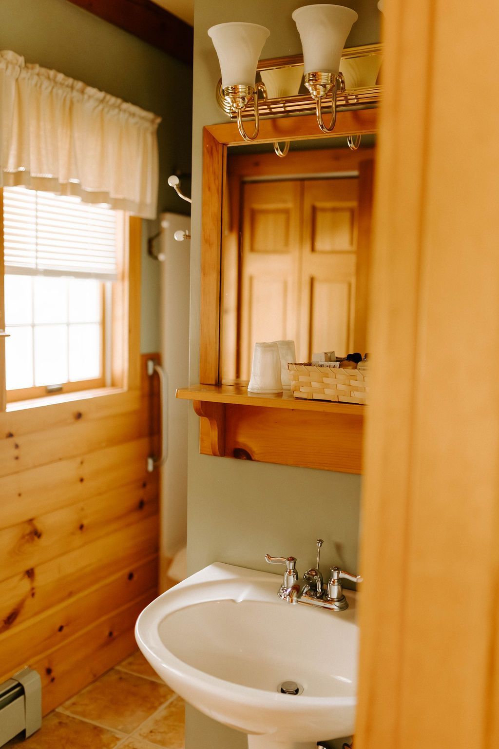 Small bathroom with wood-paneled walls, a white sink, mirror, and window with blinds.