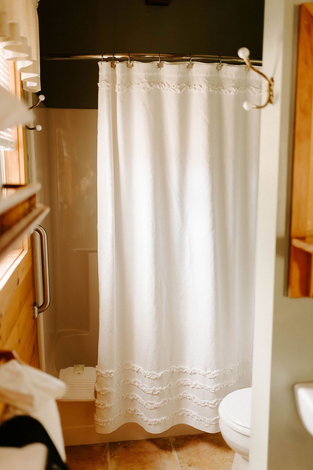 White shower curtain in a small bathroom with wood cabinets and a toilet visible on the right.