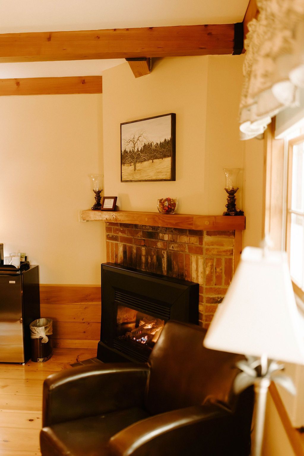 Cozy living room with a brick fireplace, black leather chair, and lamp by a window