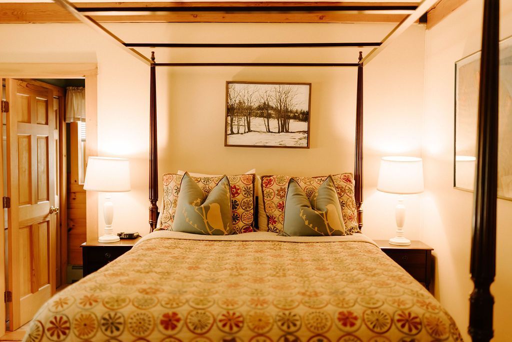 Cozy bedroom with a four-poster bed, patterned bedspread, lamps, and framed wall art