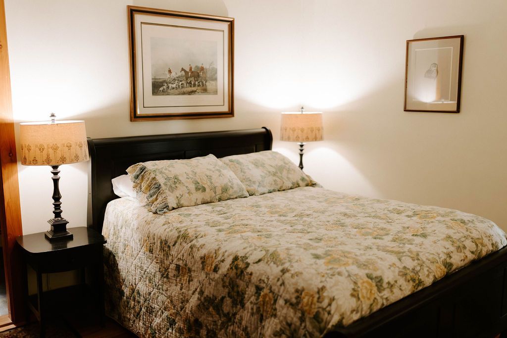 Cozy bedroom with a made bed, floral comforter, bedside lamps, and framed wall art.