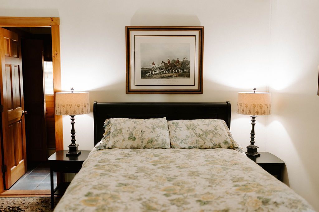 Bedroom with a made bed, bedside lamps, framed wall art, and an open wooden door