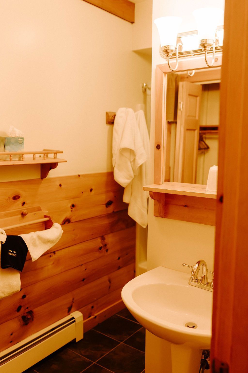 Small bathroom with sink, mirror, towel, and wood-paneled walls; toilet partially visible on the left.