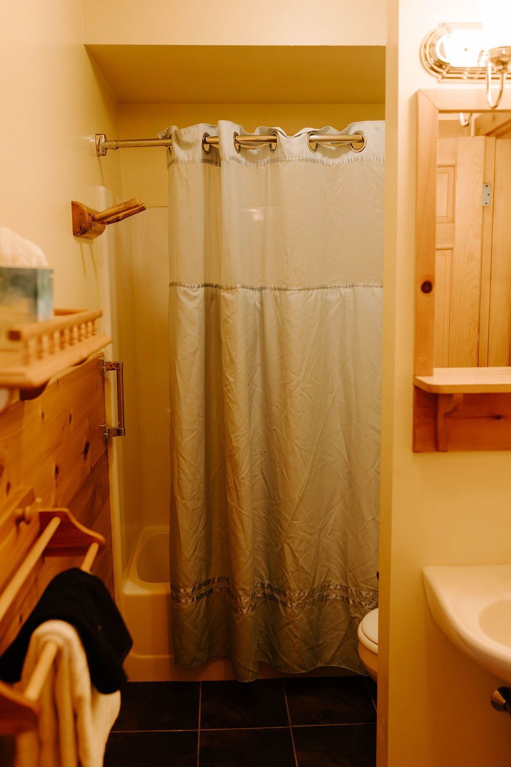 Small bathroom with a white shower curtain, beige walls, dark tile floor, and a sink and towel rack on the right.
