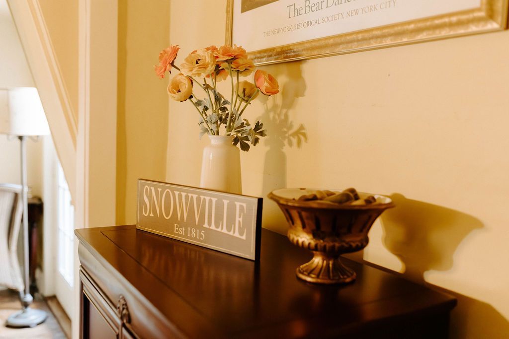 Decorated hallway table with flowers, a Snowville sign, and a decorative bowl beneath framed wall art