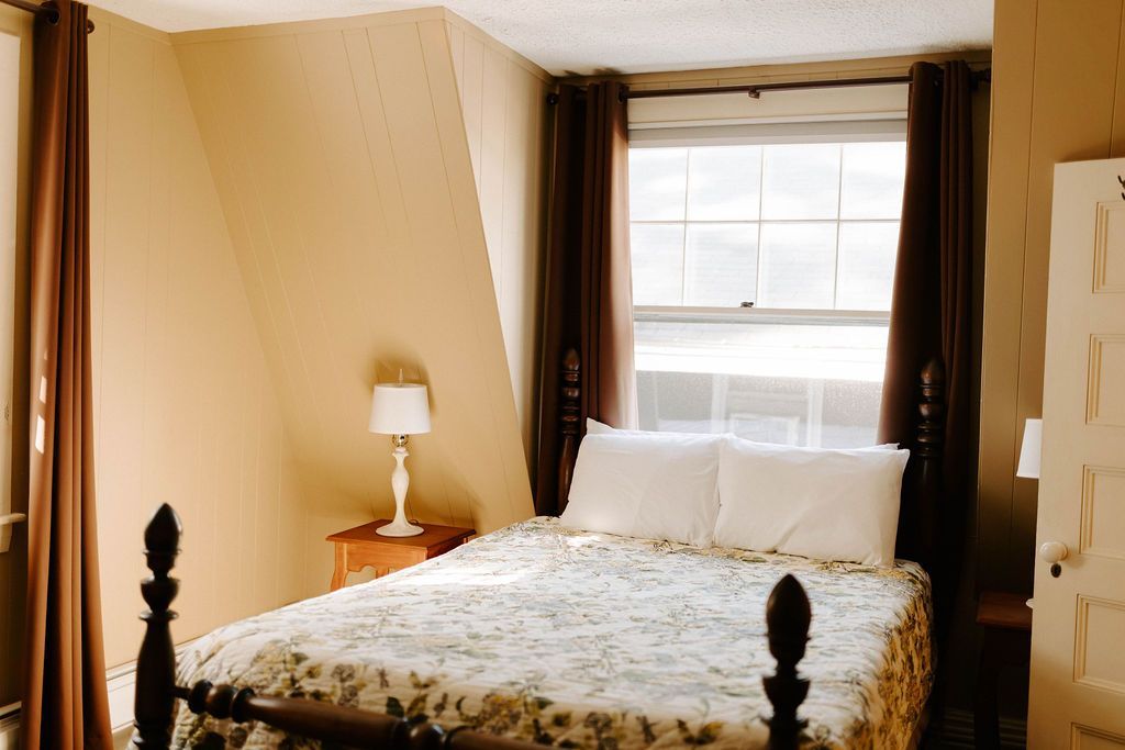 Cozy bedroom with a four-poster bed, bedside lamp, and sunlit window with dark curtains