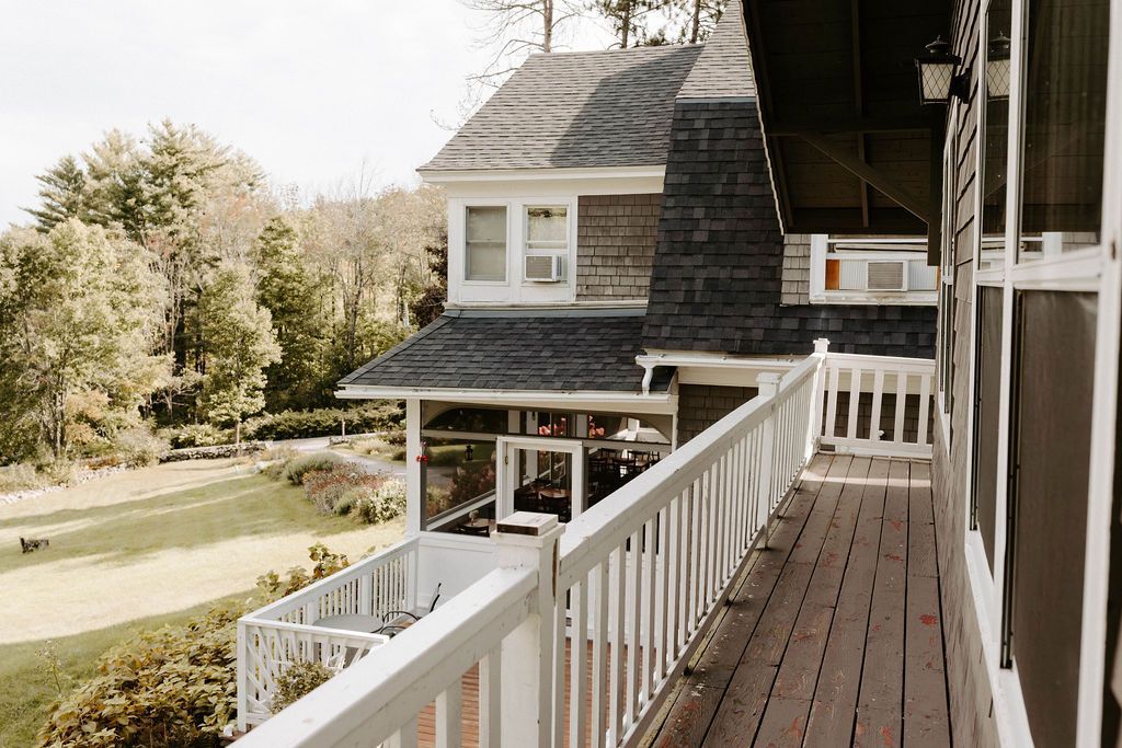Porch walkway beside a gray house with white railings and trees beyond