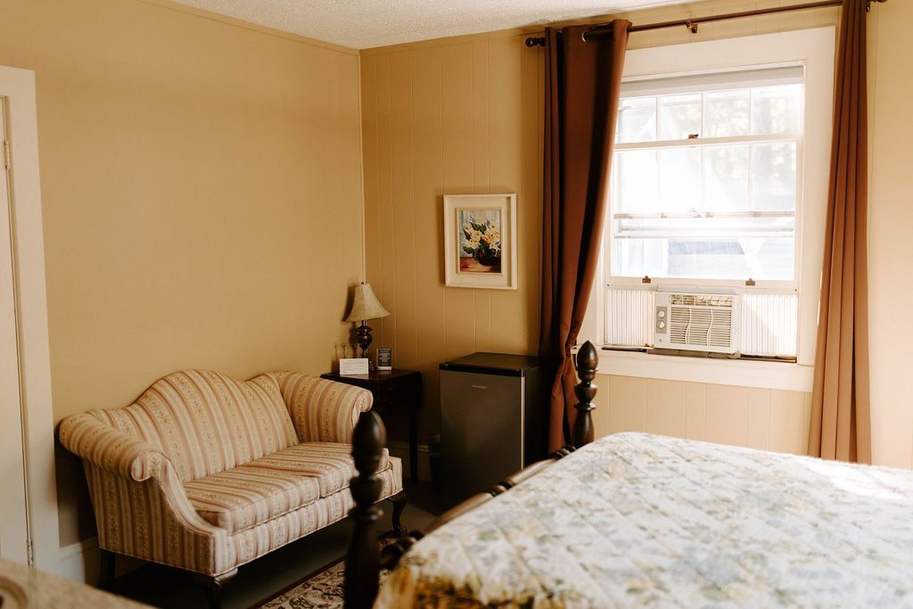 Cozy bedroom with a striped loveseat, bed, window with curtains, and warm beige walls