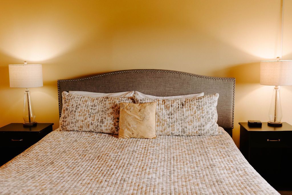 Neatly made bed with patterned bedding and two bedside lamps in a warm, softly lit bedroom