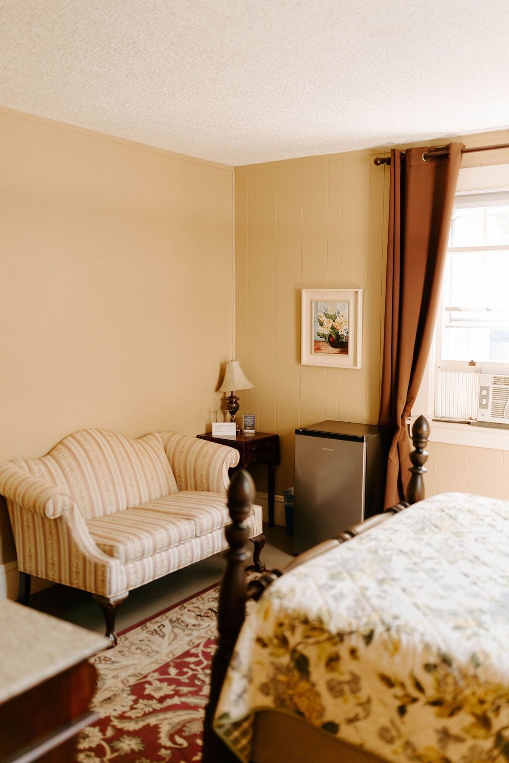 Cozy bedroom with striped armchair, bedside table, framed art, and window with brown curtains.