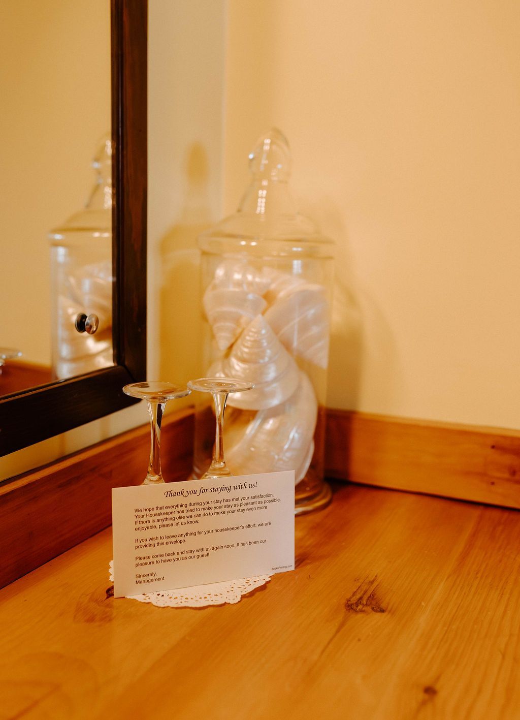 Glass jar with a small figurine and a note card on a wooden floor beside a mirror