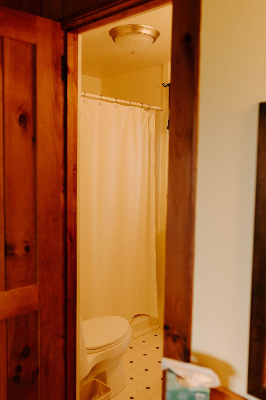 Partially open bathroom door with toilet and white shower curtain visible