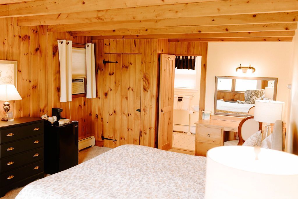 Wood-paneled bedroom with a bed, dresser, lamp, and vanity mirror