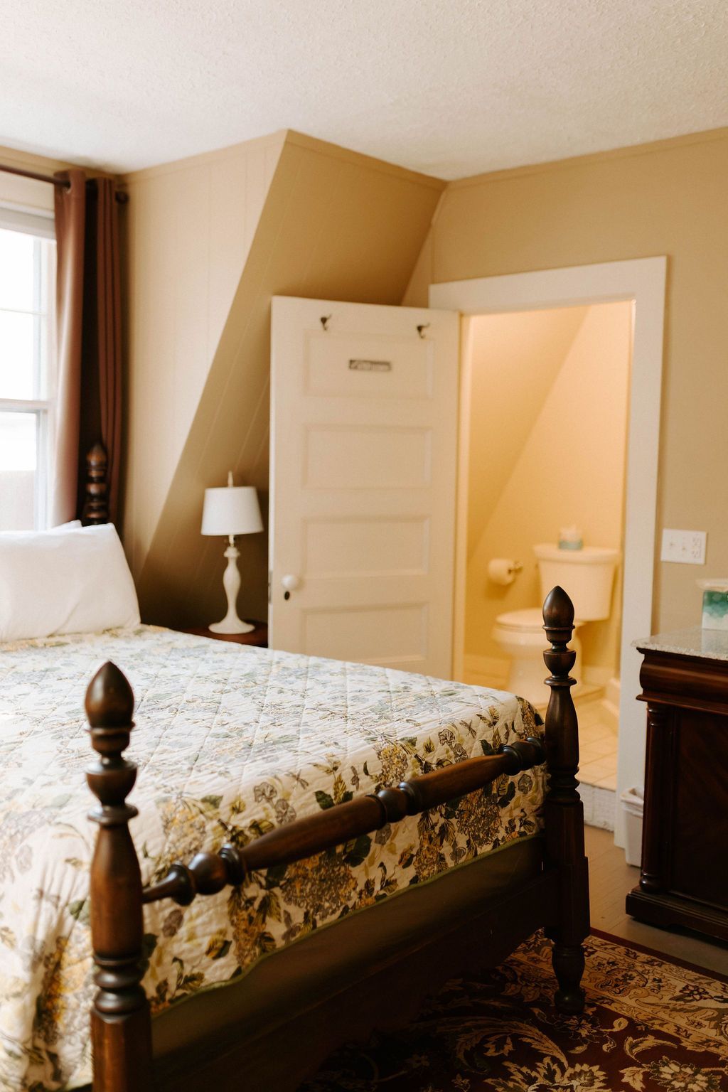 Bedroom with a wooden bed, white lamp, open door, and warm beige walls.