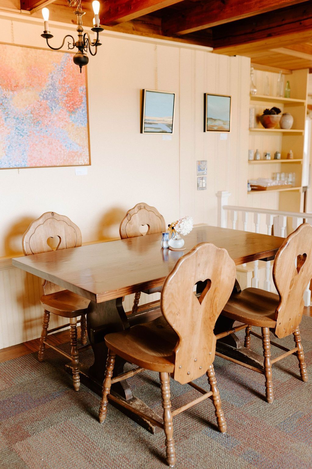 Dining room with wooden table and carved chairs, wall art, shelf, and exposed ceiling beams