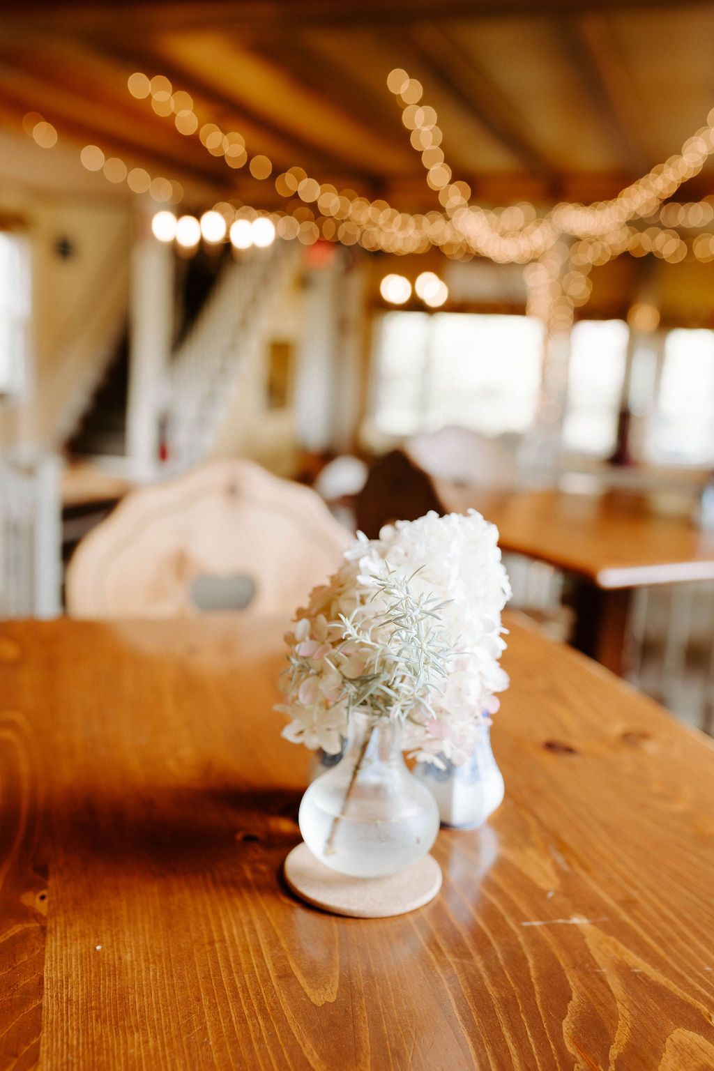Small white floral arrangement in a vase on a wooden table in a softly lit rustic room