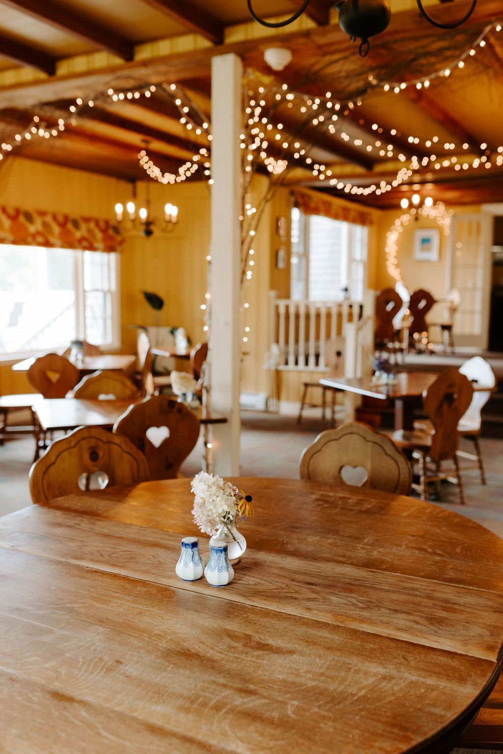Rustic dining room with wooden tables, carved chairs, and string lights under a vaulted ceiling
