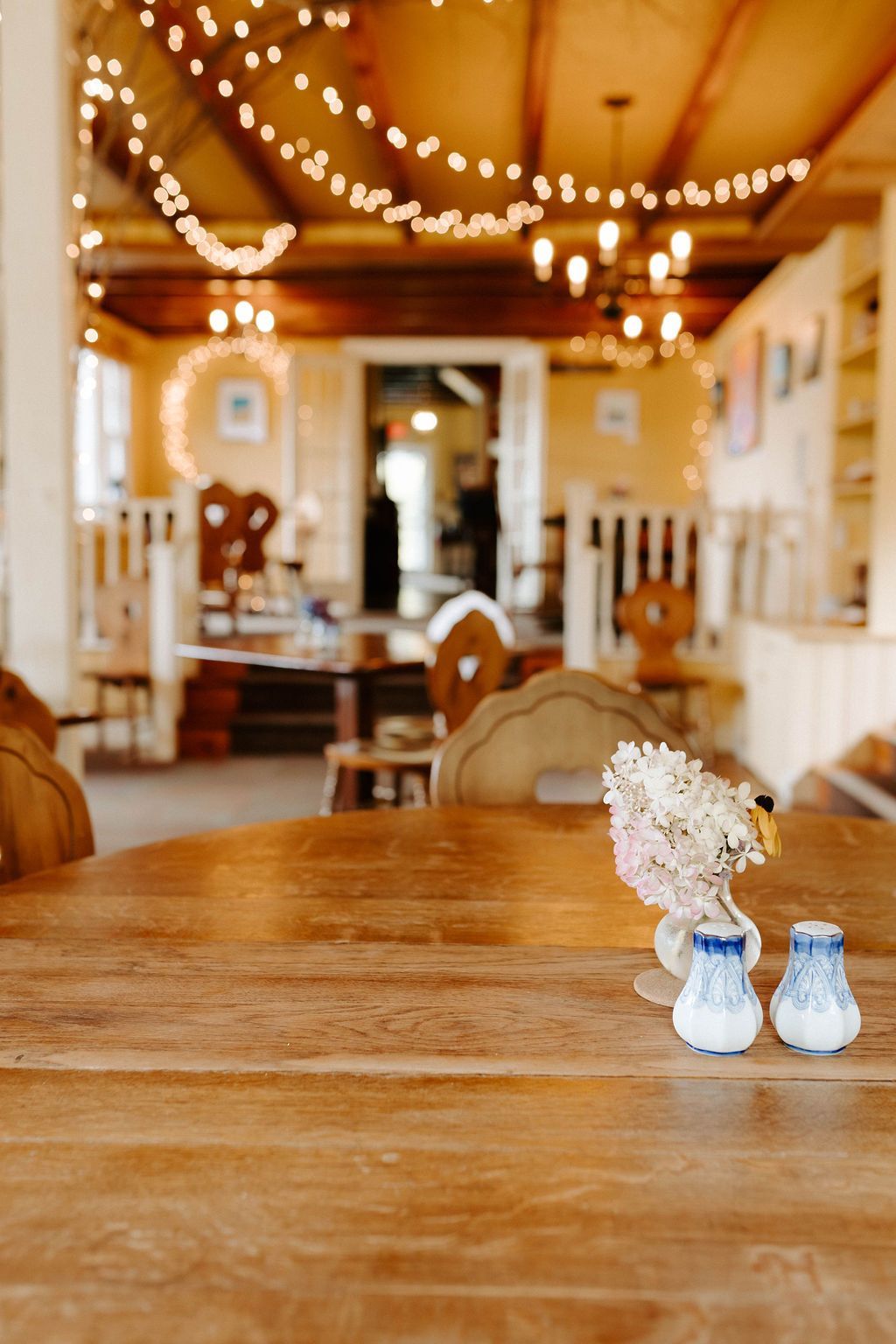 Cozy café interior with wooden tables, warm string lights, and small blue-and-white vases on a table