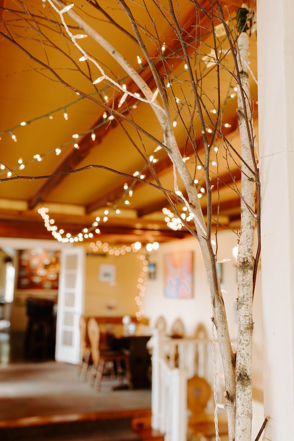 Birch branches and string lights decorating a warm indoor café with an orange ceiling