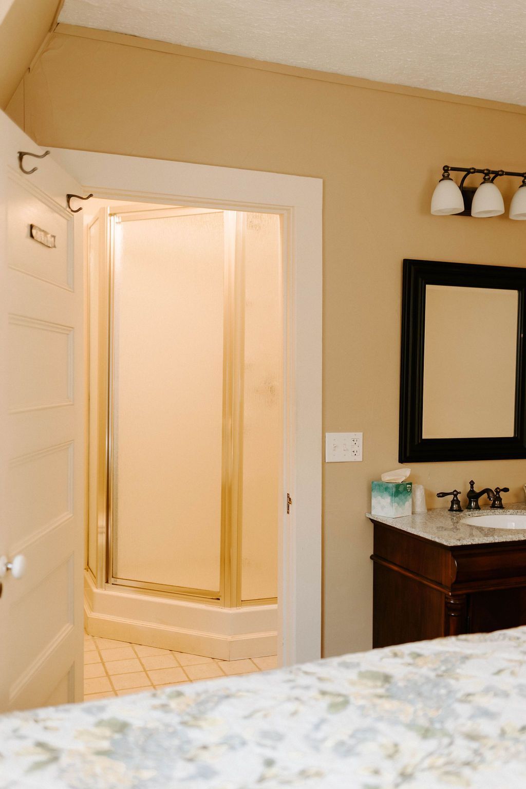 Bathroom with open shower door, beige walls, and a vanity with black-framed mirror.