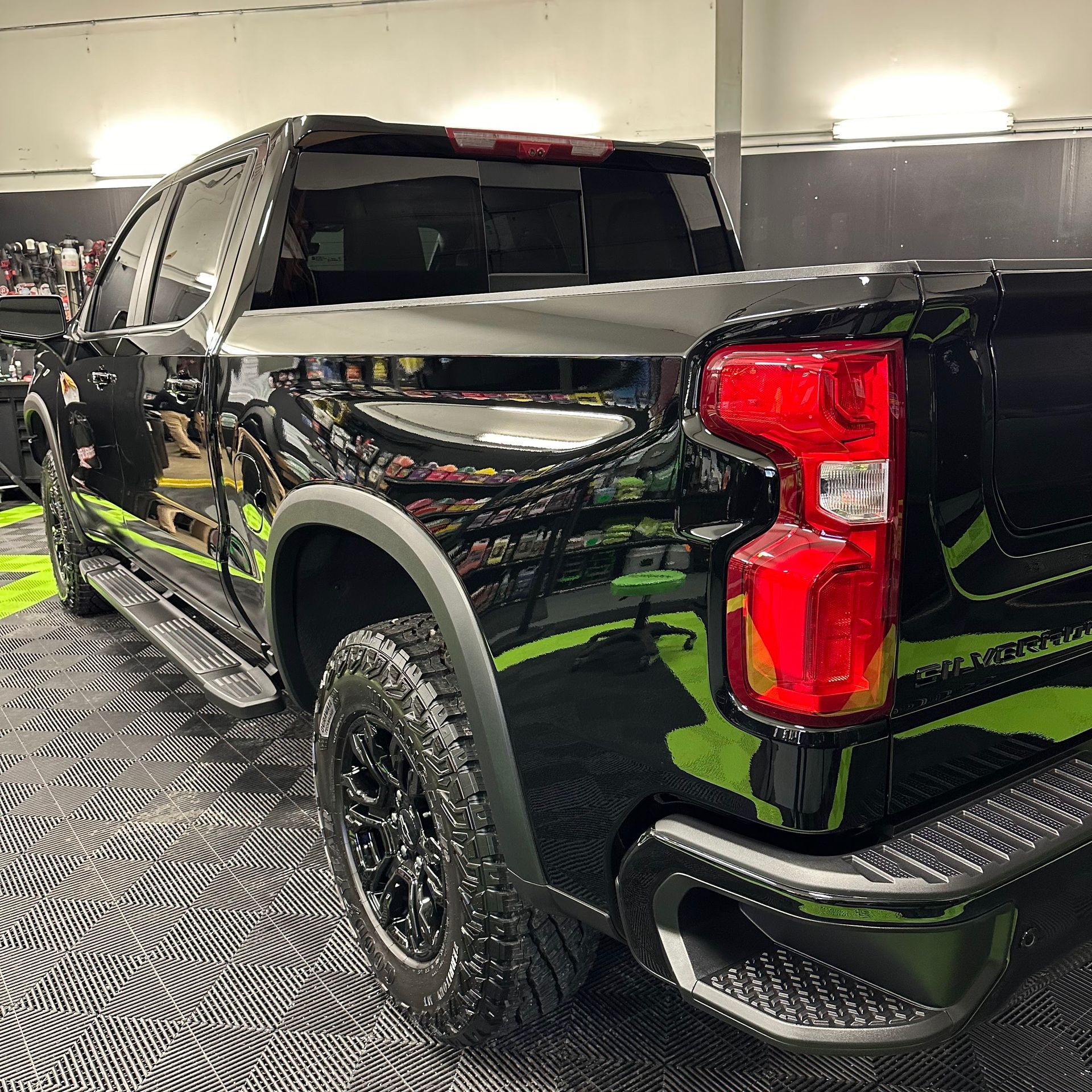 Black pickup truck with black tires, parked on a patterned floor, inside a garage.