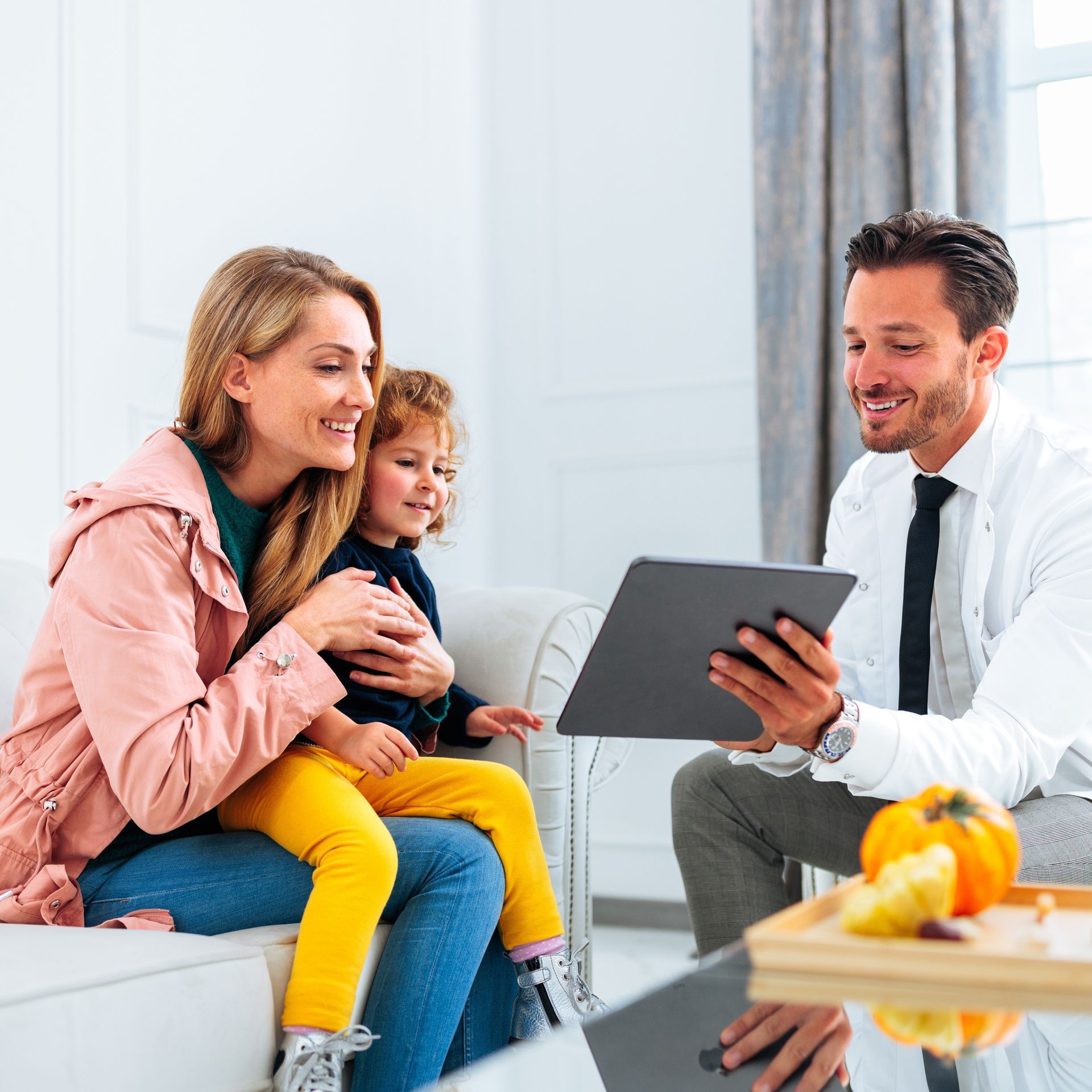Doctor sitting with woman and child, showing information on tablet
