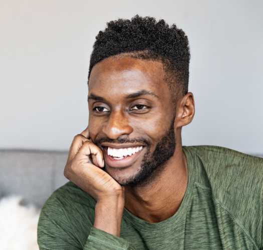 A man with a beard is smiling with his hand on his chin.