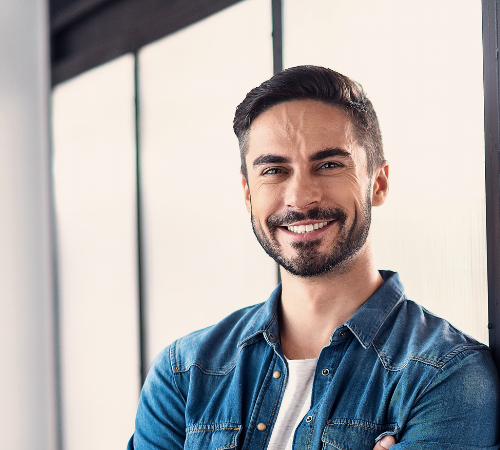 A man with a beard is smiling for the camera while leaning against a wall.