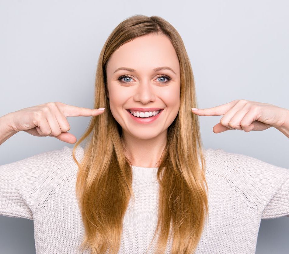 A woman is smiling and pointing at her teeth.