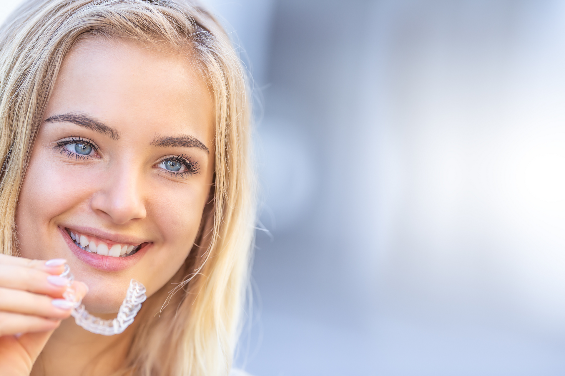 A woman is smiling while holding a clear brace on her teeth.