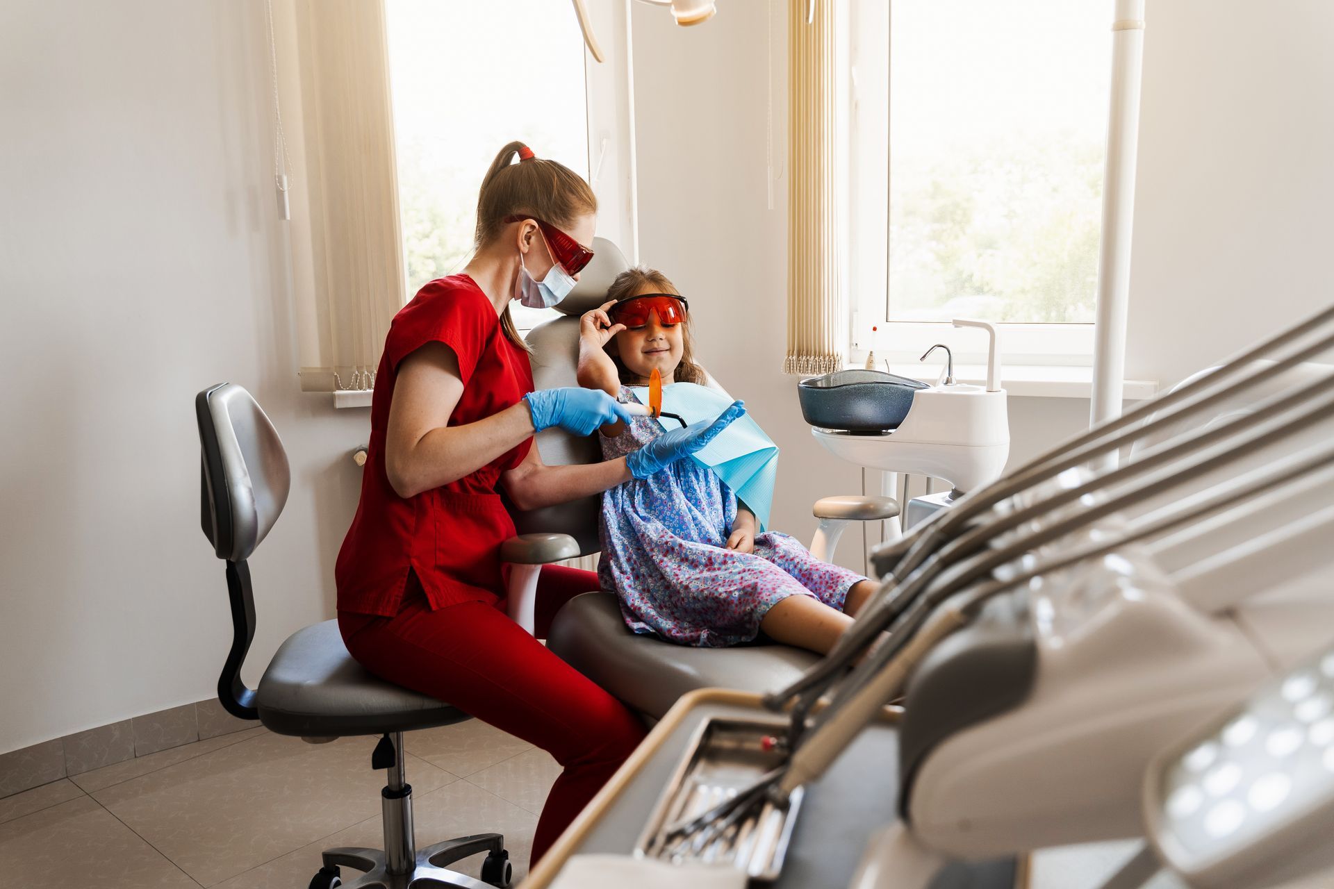 Dentist in red scrubs, attending to a child in a dental chair, dental office.