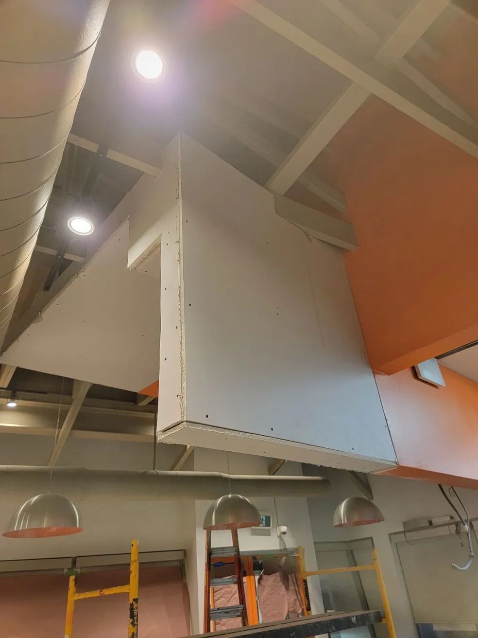 Nouvelles structures de plafond en plaques de plâtre et luminaires installés dans une pièce aux murs orange et aux échafaudages jaunes.