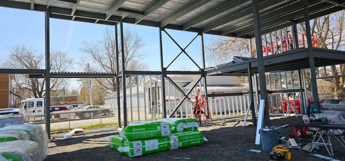 Vue intérieure d'un bâtiment en construction, montrant la charpente métallique apparente, le platelage métallique et l'isolation.