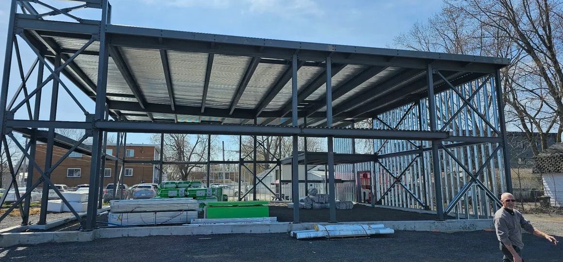 Une structure à ossature métallique en construction sur un chantier extérieur, avec un ouvrier debout au premier plan.