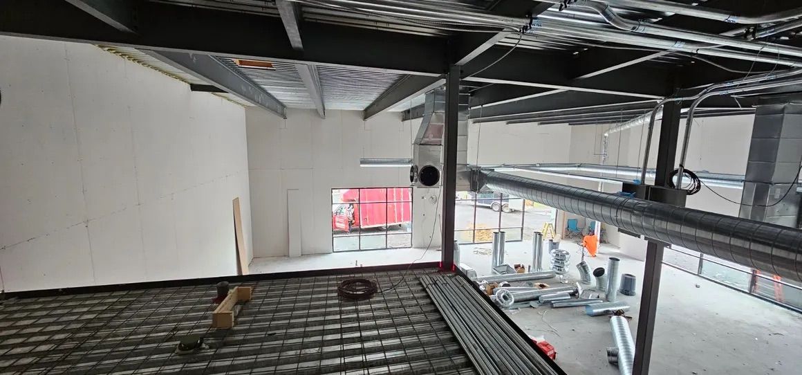 Vue aérienne d'un bâtiment en construction, montrant des poutres d'acier apparentes, un platelage métallique et des conduits de ventilation.