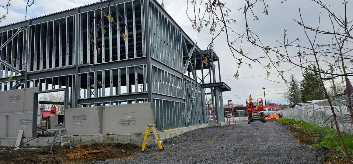 Chantier de construction présentant une structure de bâtiment à deux étages composée de montants en acier, avec des blocs de béton à la base.