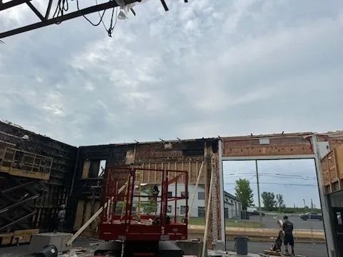 Des ouvriers du bâtiment et des engins lourds à l'intérieur de la structure métallique d'un bâtiment en rénovation, sous un ciel nuageux.