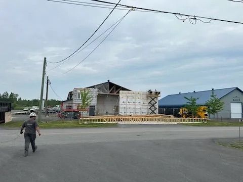 Un ouvrier du bâtiment s'approche d'un bâtiment en rénovation dont la charpente en bois est apparente et les murs extérieurs partiellement délabrés.