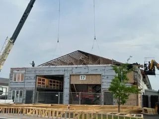 Une grue dépose une grande charpente de toit en bois sur la façade inachevée d'un bâtiment portant le numéro 17.