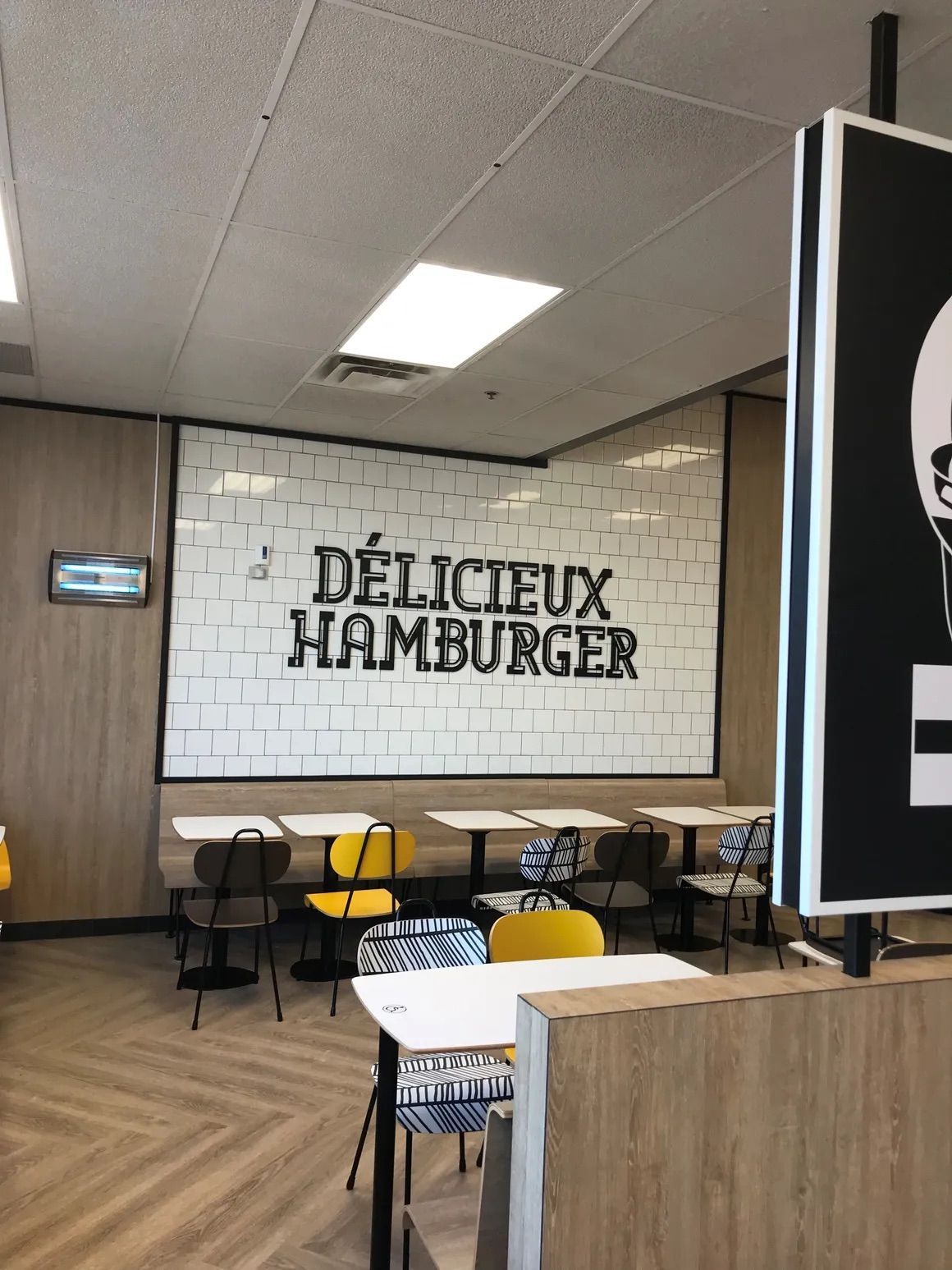 L'intérieur d'un restaurant avec des chaises jaunes à motifs autour des tables, et l'inscription « DÉLICIEUX HAMBURGER » sur un mur.